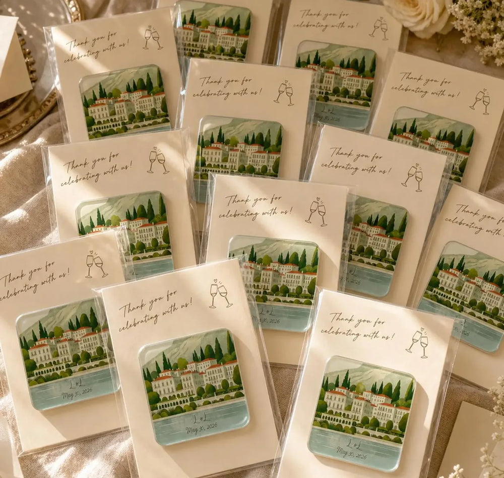 Illustrated lakeside villa magnets with matching cream cards arranged beside flowers and fabric.